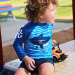 Load image into Gallery viewer, Child wearing a blue and white shark-patterned shirt sitting on a playground.
