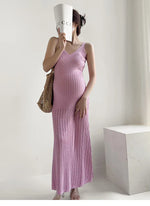 Load image into Gallery viewer, A pregnant woman wearing a light pink textured knit maxi slip dress, holding a white Gucci-branded paper cup to her face and carrying a woven straw tote bag, standing in a minimalist white room.

