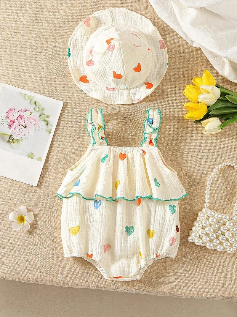 Baby romper with heart patterns, hat, and flowers on a textured surface