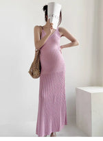 Load image into Gallery viewer, A pregnant woman wearing a pink ribbed knit maxi dress, holding a white Gucci-branded cup to her face and carrying a woven straw bag, set against a minimalist white background.
