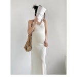 Load image into Gallery viewer, A pregnant woman wearing a white ribbed knit maxi dress, holding a white Gucci-branded paper cup to her face and carrying a beige woven tote bag against a plain light gray wall.
