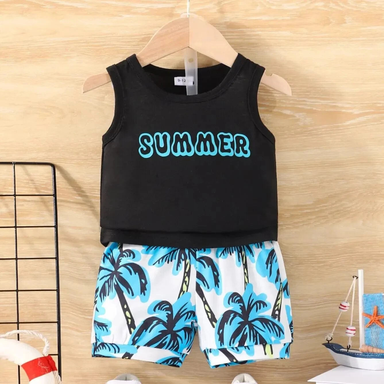Black sleeveless top with 'SUMMER' text and palm tree shorts on a wooden surface.