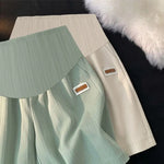 Load image into Gallery viewer, Two pieces of clothing, one green and one beige, with labels on a dark surface.
