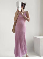 Load image into Gallery viewer, A woman models a sleeveless, textured knit maxi dress in a dusty pink shade. She is holding a white paper cup with the brand name 'GUCCI' printed on it, and carrying a woven straw shoulder bag, set against a minimalist white studio background with a white block prop.

