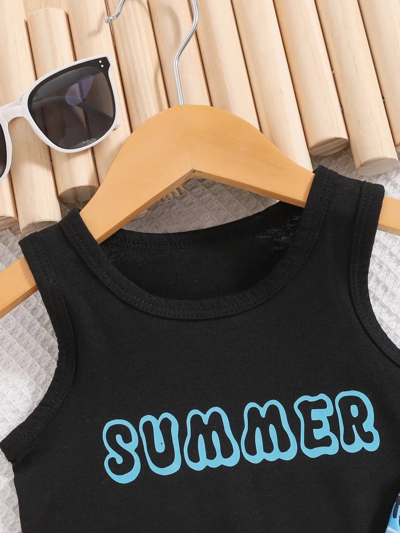 Black tank top with 'SUMMER' text in blue on a hanger with sunglasses in the background.
